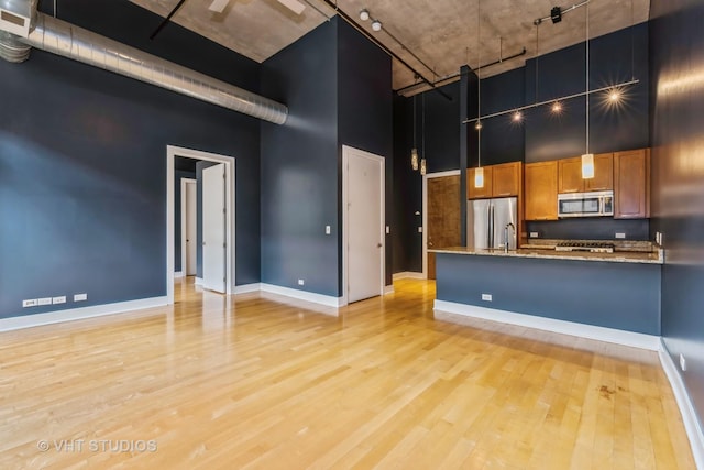 kitchen with a towering ceiling, light stone counters, stainless steel appliances, and light hardwood / wood-style floors