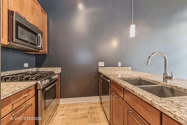 kitchen with light stone counters, sink, hanging light fixtures, and appliances with stainless steel finishes