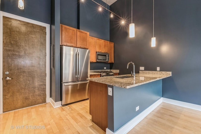 kitchen with kitchen peninsula, appliances with stainless steel finishes, a towering ceiling, hanging light fixtures, and sink