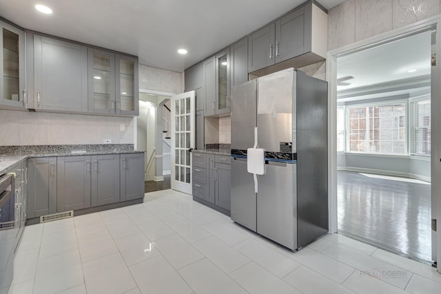 kitchen featuring stainless steel refrigerator, decorative backsplash, dark stone countertops, and gray cabinetry