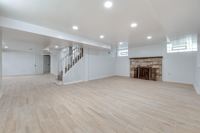 basement with a stone fireplace, a wealth of natural light, and light hardwood / wood-style flooring