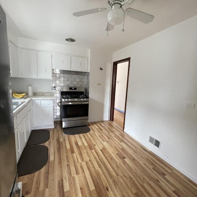 kitchen featuring gas range, white cabinetry, decorative backsplash, and light wood-type flooring