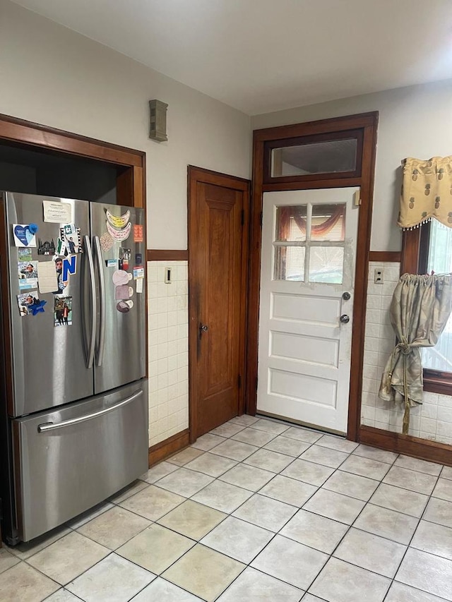 kitchen featuring stainless steel fridge, light tile patterned floors, and tile walls