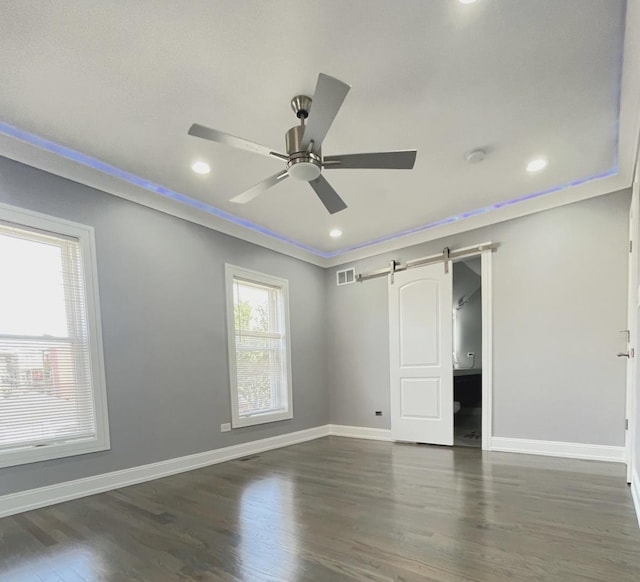 unfurnished bedroom featuring a barn door, ceiling fan, dark hardwood / wood-style flooring, and ornamental molding