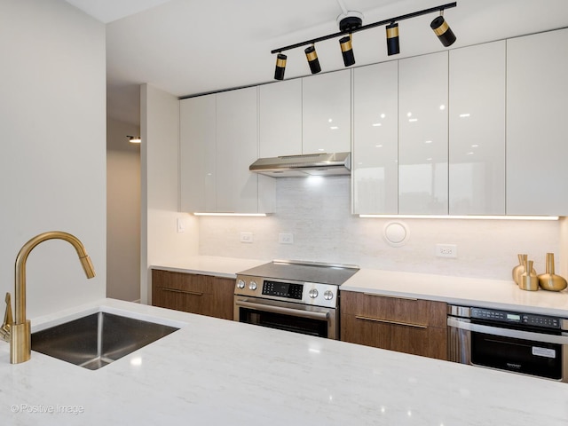 kitchen featuring white cabinetry, sink, light stone countertops, stainless steel appliances, and backsplash