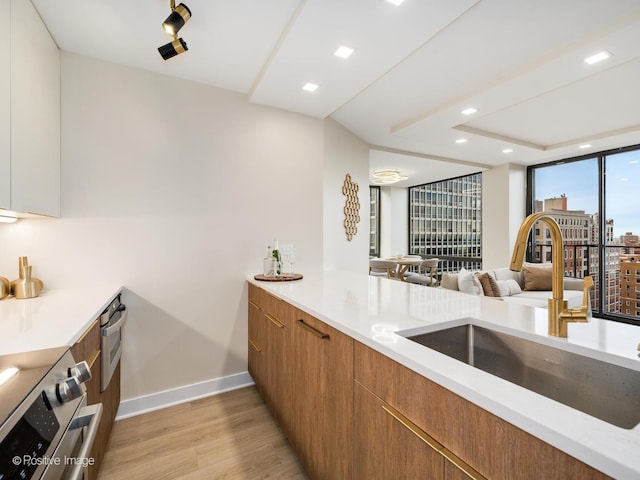 kitchen with electric stove, sink, expansive windows, and light hardwood / wood-style flooring