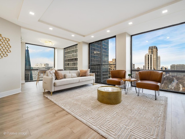 living room featuring a tray ceiling, floor to ceiling windows, and light hardwood / wood-style floors