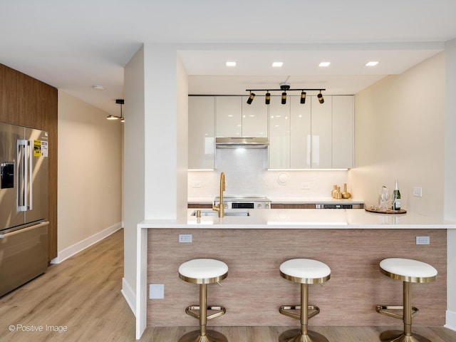 kitchen featuring kitchen peninsula, a kitchen breakfast bar, high quality fridge, light hardwood / wood-style floors, and white cabinetry