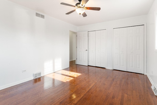 unfurnished bedroom featuring ceiling fan, wood-type flooring, and two closets