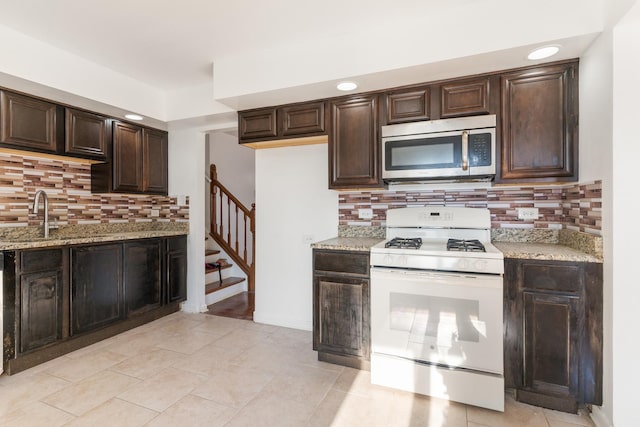 kitchen with backsplash, white stove, sink, light stone countertops, and dark brown cabinets