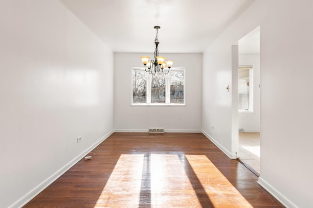 unfurnished dining area featuring a notable chandelier, plenty of natural light, and dark wood-type flooring