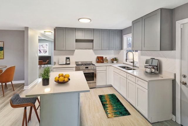 kitchen featuring sink, light hardwood / wood-style flooring, gray cabinets, a breakfast bar area, and stainless steel range with gas stovetop