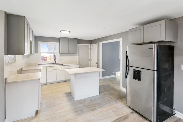 kitchen featuring stainless steel refrigerator, a center island, gray cabinets, and sink