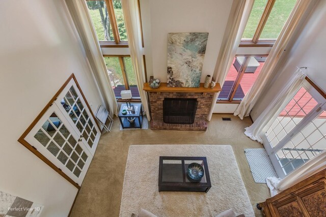 carpeted living room featuring plenty of natural light, a high ceiling, and a brick fireplace