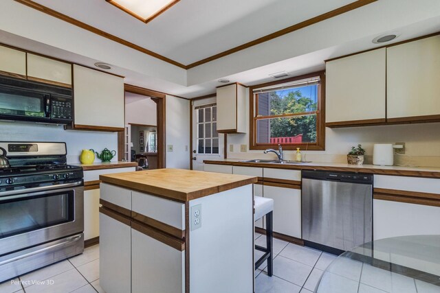 kitchen featuring sink, light tile patterned floors, ornamental molding, appliances with stainless steel finishes, and a kitchen island