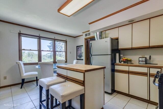 kitchen with a kitchen bar, stainless steel fridge, wood counters, a center island, and white cabinetry