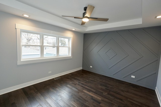 empty room with dark wood-type flooring, a raised ceiling, and ceiling fan