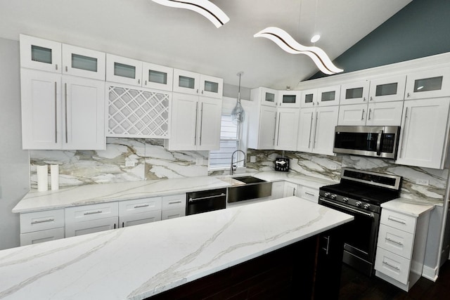 kitchen with stainless steel appliances, white cabinets, vaulted ceiling, and hanging light fixtures