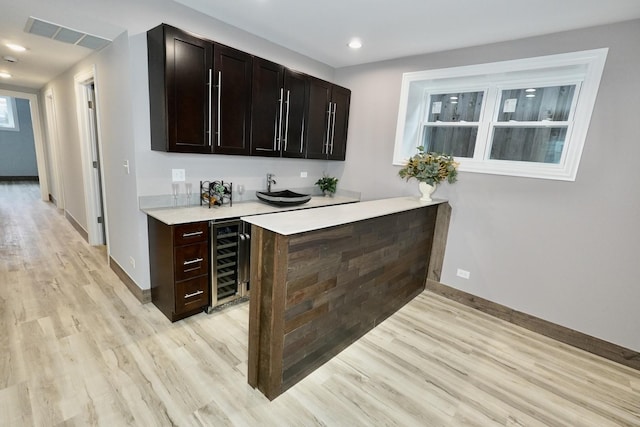 bar featuring light hardwood / wood-style floors, beverage cooler, and dark brown cabinetry