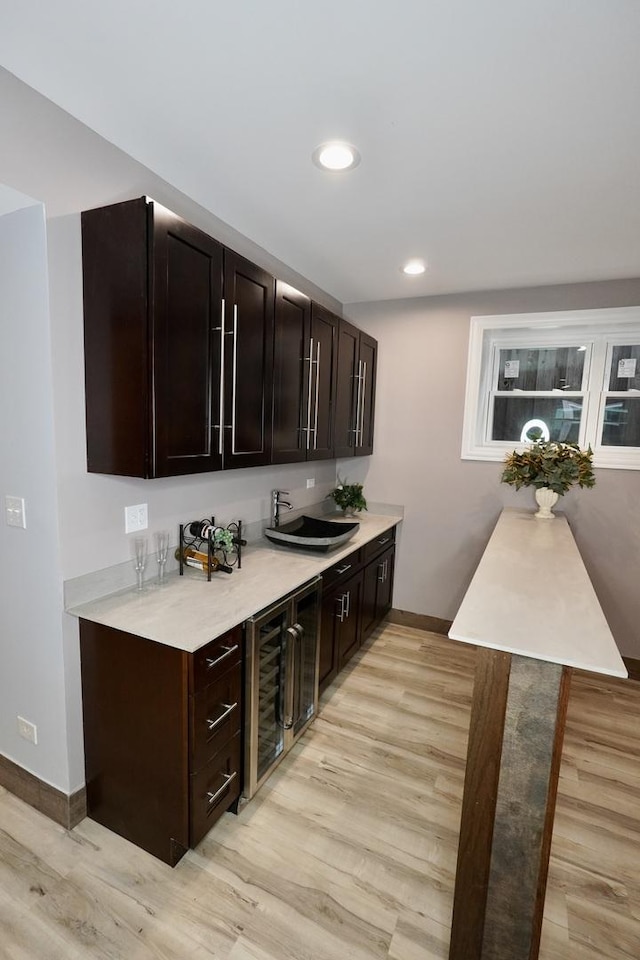 bar with dark brown cabinetry, wine cooler, and light hardwood / wood-style flooring