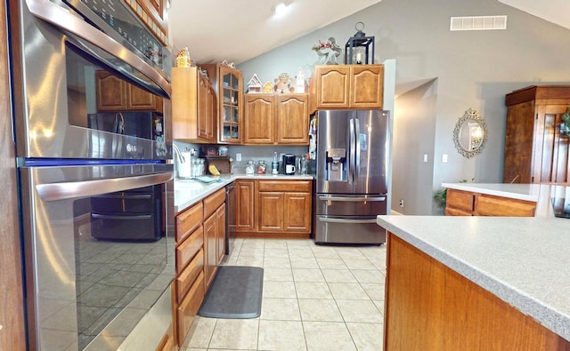 kitchen with appliances with stainless steel finishes, lofted ceiling, and light tile patterned flooring