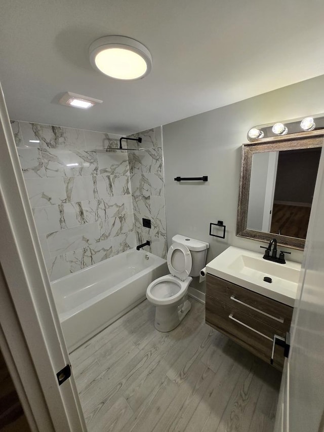 full bathroom featuring vanity, hardwood / wood-style floors, tiled shower / bath combo, and toilet