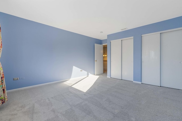 unfurnished bedroom featuring multiple closets and light colored carpet