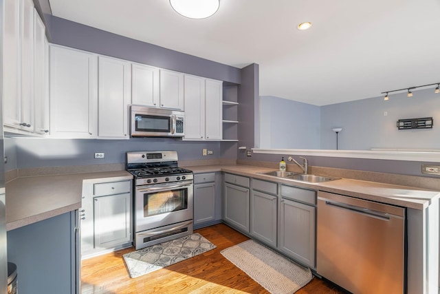 kitchen with sink, gray cabinets, stainless steel appliances, light hardwood / wood-style floors, and white cabinets