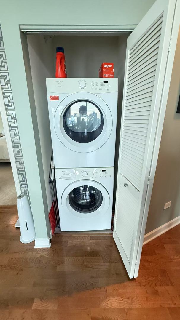 laundry room with stacked washing maching and dryer and dark hardwood / wood-style floors