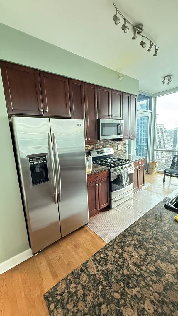 kitchen featuring floor to ceiling windows, dark stone counters, dark brown cabinetry, stainless steel appliances, and light hardwood / wood-style floors