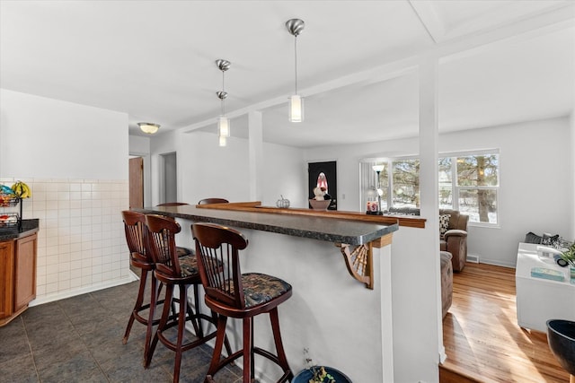 kitchen with kitchen peninsula, a breakfast bar, hanging light fixtures, and tile walls