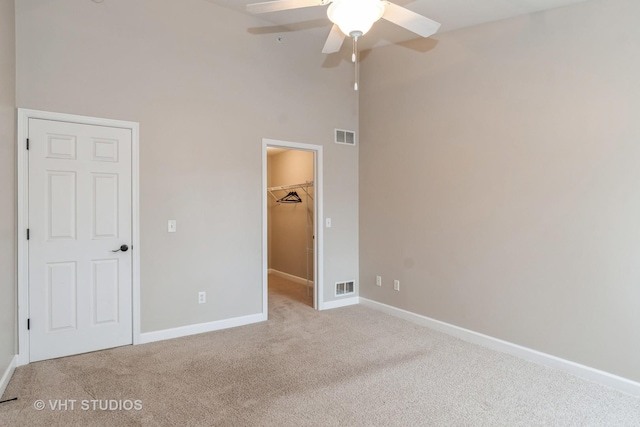 unfurnished bedroom with a towering ceiling, light colored carpet, ceiling fan, a spacious closet, and a closet