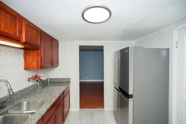 kitchen featuring decorative backsplash, stainless steel fridge, sink, and dark stone counters