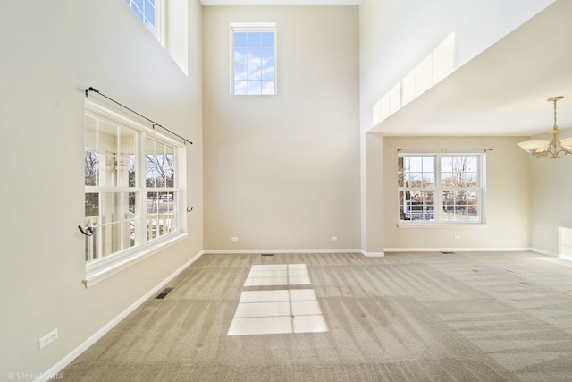 unfurnished living room featuring plenty of natural light, a towering ceiling, light carpet, and a notable chandelier