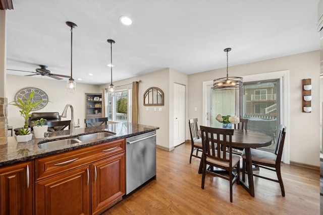 kitchen featuring decorative light fixtures, dark stone countertops, stainless steel dishwasher, sink, and light wood-type flooring