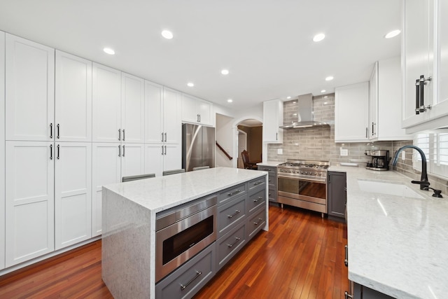 kitchen with appliances with stainless steel finishes, white cabinets, a center island, light stone countertops, and wall chimney range hood