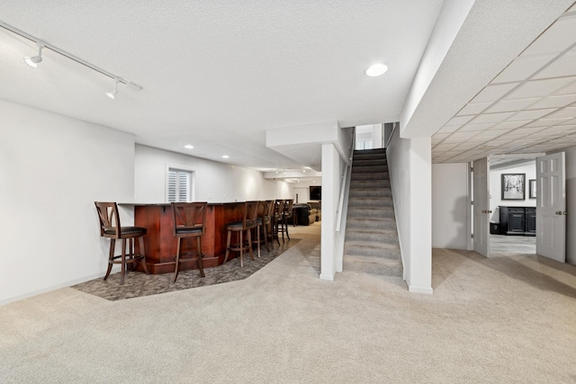 bar featuring light colored carpet, rail lighting, and a textured ceiling