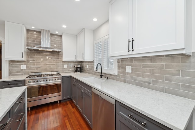 kitchen with wall chimney exhaust hood, sink, white cabinetry, stainless steel appliances, and light stone countertops