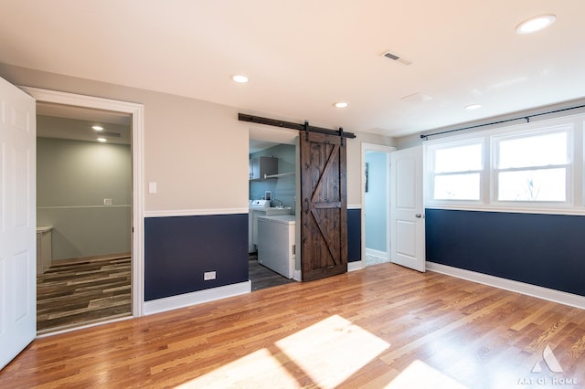 unfurnished bedroom featuring hardwood / wood-style floors, ensuite bathroom, and a barn door