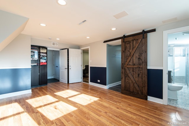 unfurnished bedroom with a barn door, wood-type flooring, connected bathroom, and a closet