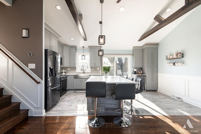 kitchen featuring gray cabinetry, refrigerator with ice dispenser, beam ceiling, pendant lighting, and a center island