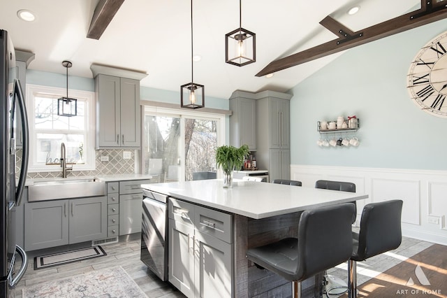 kitchen featuring stainless steel refrigerator, gray cabinetry, sink, lofted ceiling with beams, and pendant lighting