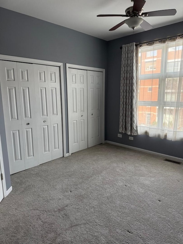 unfurnished bedroom featuring ceiling fan, multiple closets, and carpet