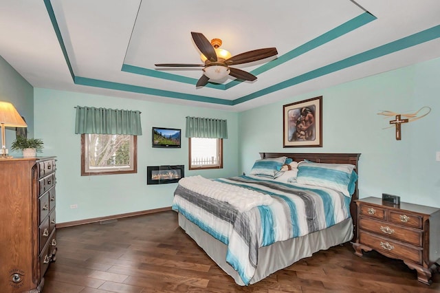 bedroom with dark hardwood / wood-style floors, a raised ceiling, and ceiling fan