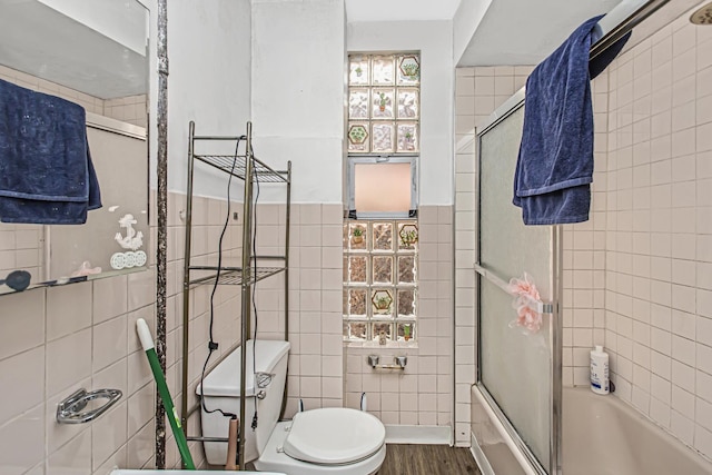 bathroom featuring wood-type flooring, toilet, enclosed tub / shower combo, and tile walls