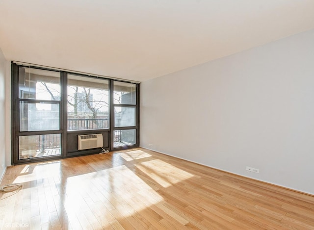 empty room with a wall mounted air conditioner, expansive windows, and light hardwood / wood-style flooring