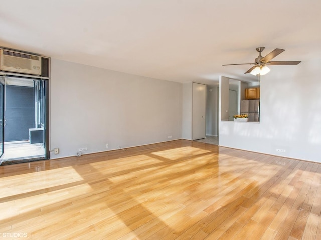 empty room featuring a wall mounted air conditioner, ceiling fan, and light hardwood / wood-style floors