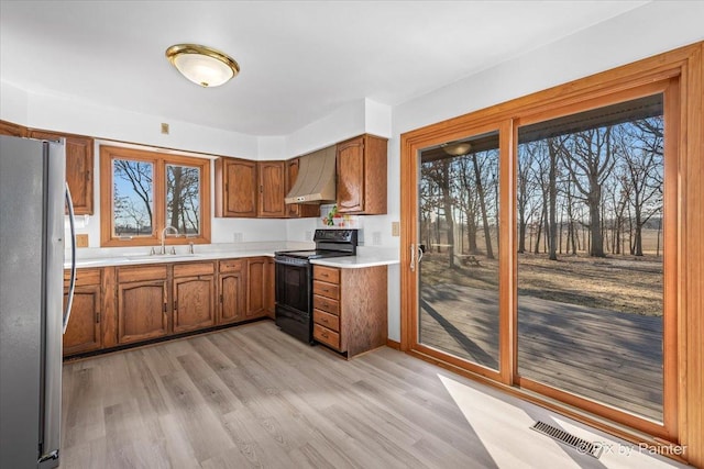 kitchen with wall chimney range hood, sink, electric range, stainless steel fridge, and light hardwood / wood-style floors