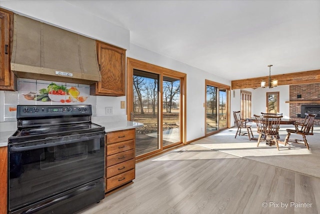 kitchen featuring a brick fireplace, black / electric stove, pendant lighting, custom exhaust hood, and light wood-type flooring