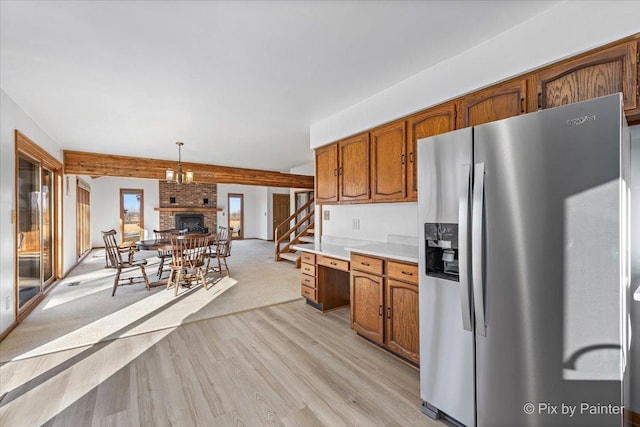 kitchen with stainless steel refrigerator with ice dispenser, light wood-type flooring, a fireplace, decorative light fixtures, and a chandelier